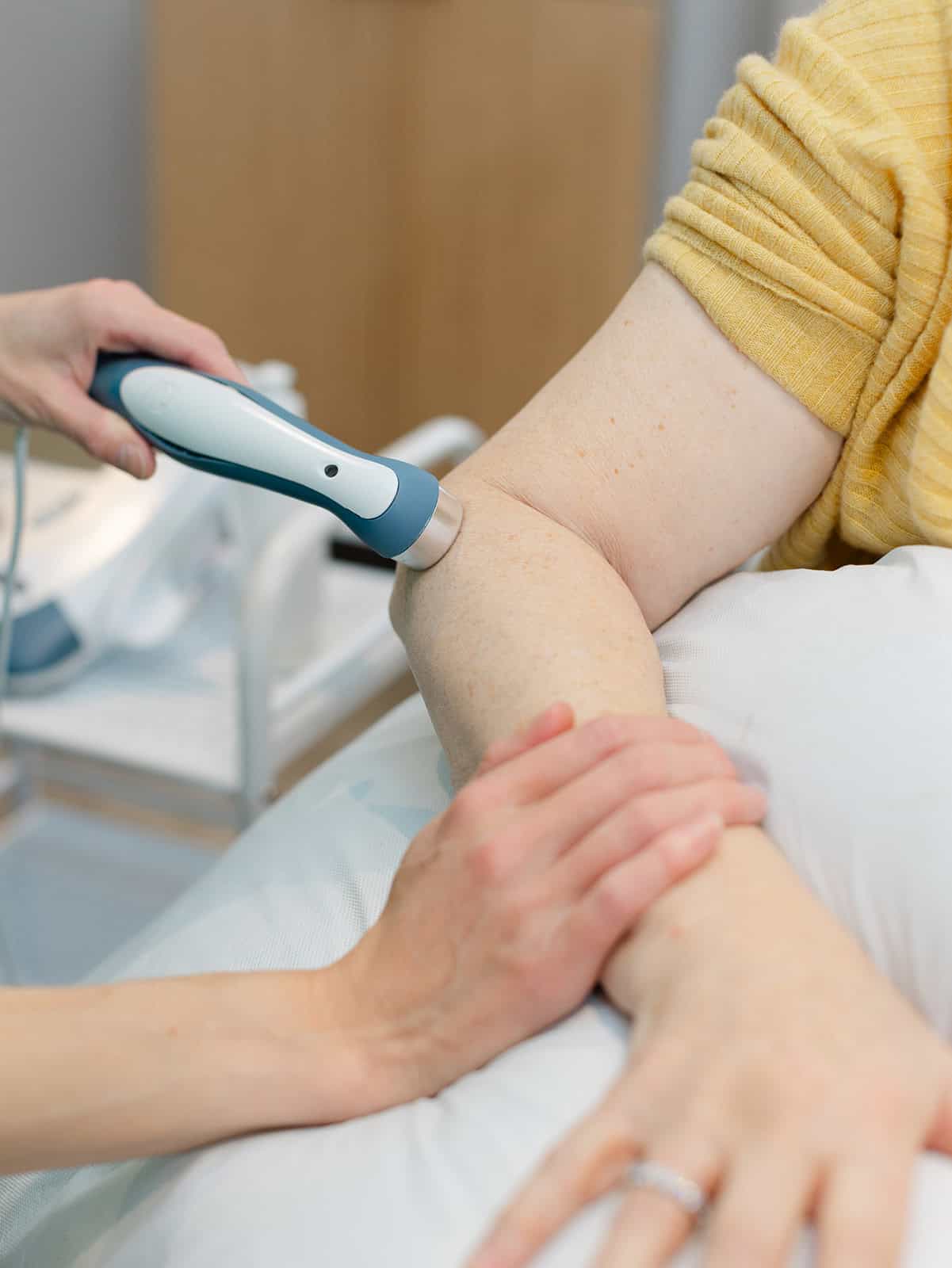 Becs Allen applying EMS 560 Radial Shockwave Unit on a client’s lower leg while on physiotherapy couch